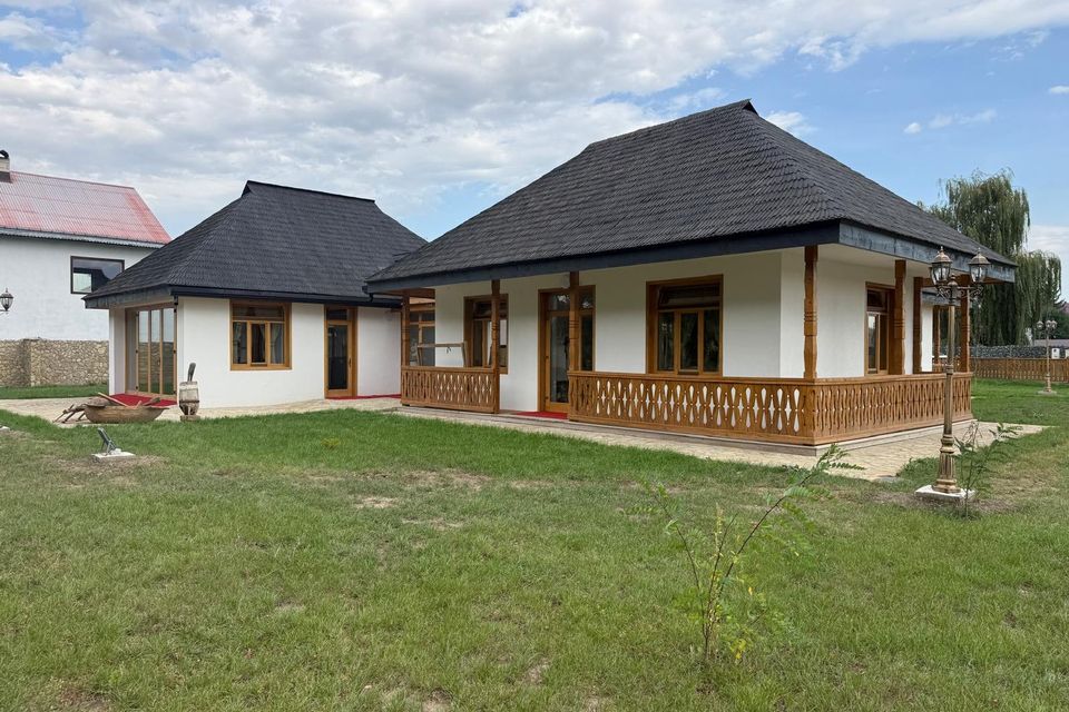 Clădirea albă a muzeului cu acoperiș de șindrilă, văzută dinspre grădină