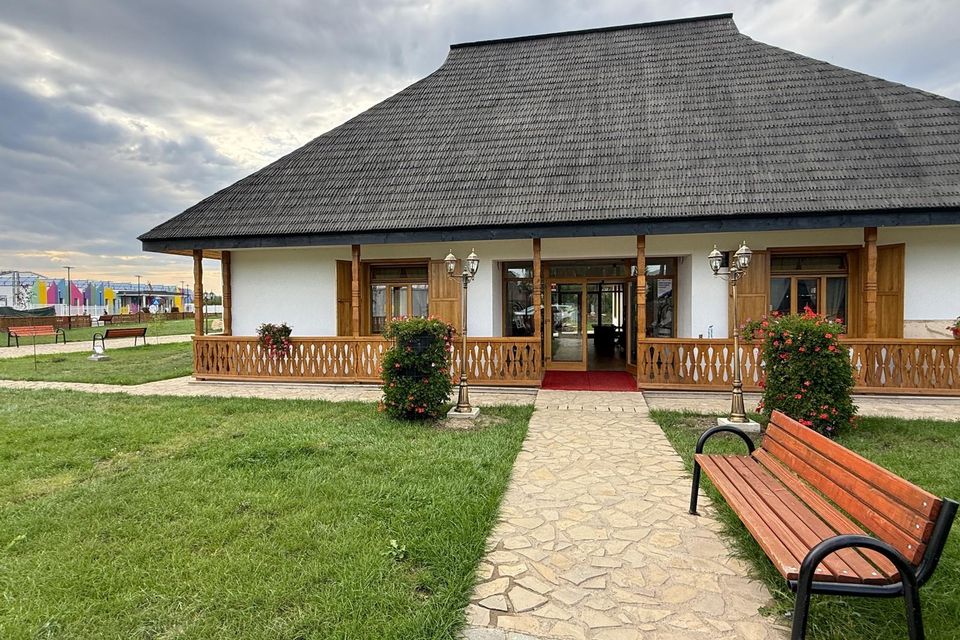 Clădirea muzeului cu pridvor de lemn, aleea pietruită și banca din curte