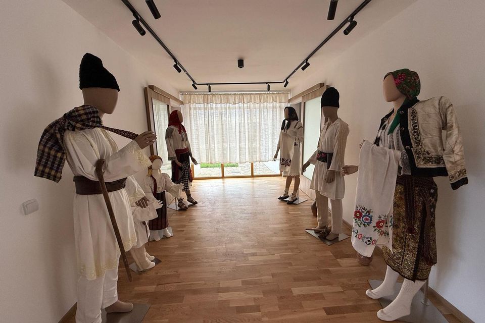Manechine cu costume populare, aliniate în sala luminoasă de expoziție
