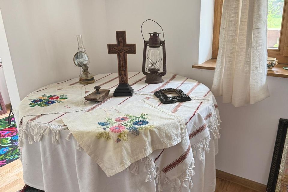 Masă rotundă cu față de masă brodată, cruce de lemn și lampă cu gaz