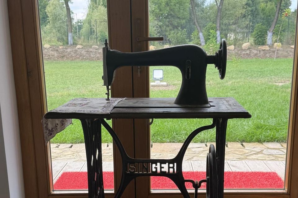 Mașină de cusut veche cu pedală, lângă ușa spre grădină